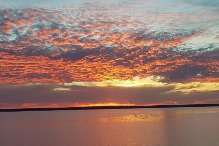Vibrant sunset over a calm lake with orange, pink, and purple clouds.