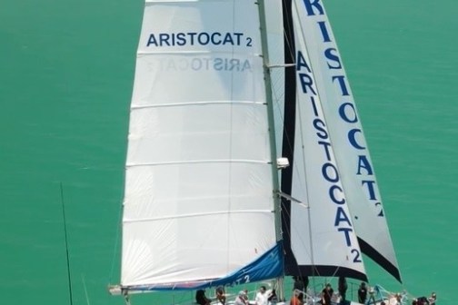Catamaran named Aristocat 2 sailing on turquoise water with passengers on deck.