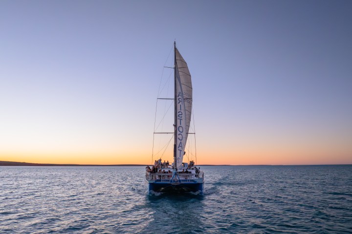Sailing boat on ocean at sunset with clear sky and calm water.