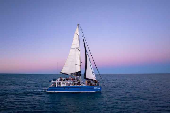 Sailboat on calm ocean with pink and blue sky at sunset.