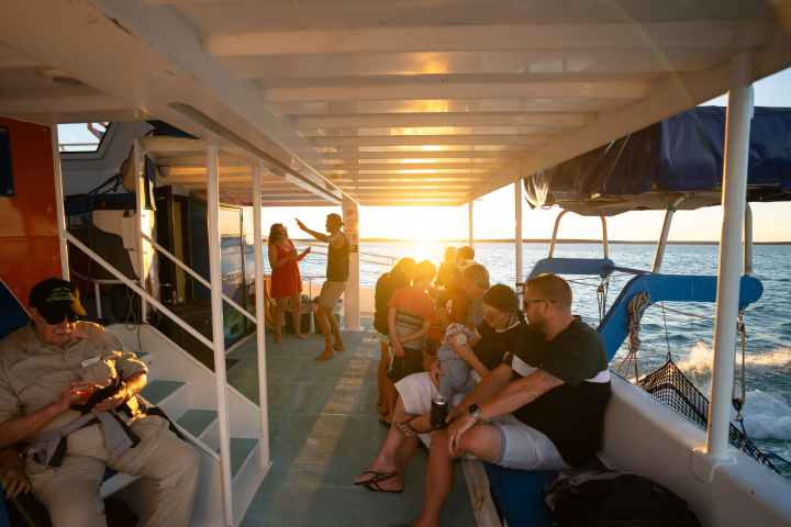 People relaxing and dancing on a boat during sunset over the ocean.