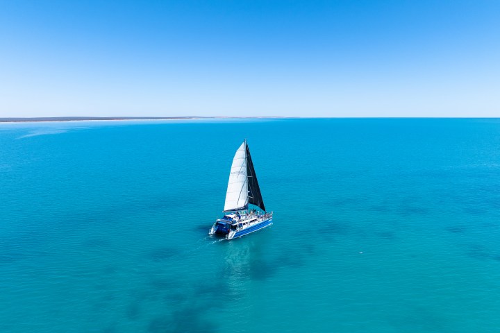 A sailboat with a black sail on calm turquoise waters under a clear blue sky.