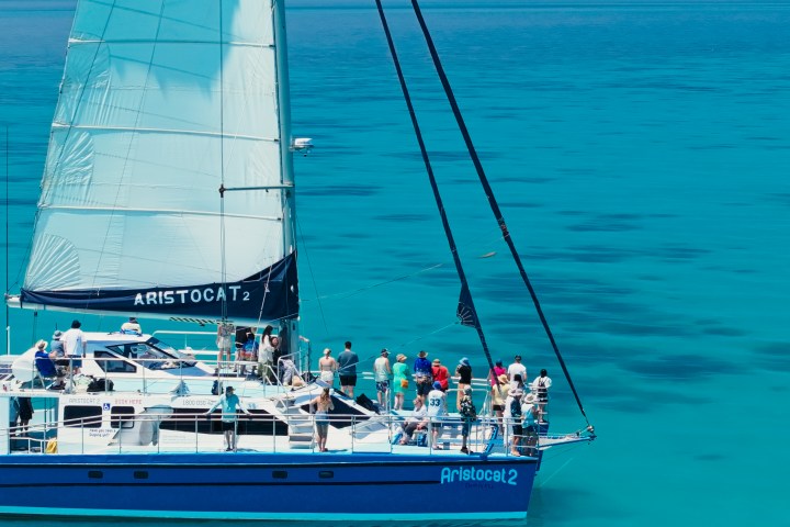 Tourists on a blue sailing boat named Aristocat 2 in clear turquoise water.