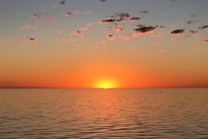 Sunset over calm ocean with orange sky and scattered clouds.