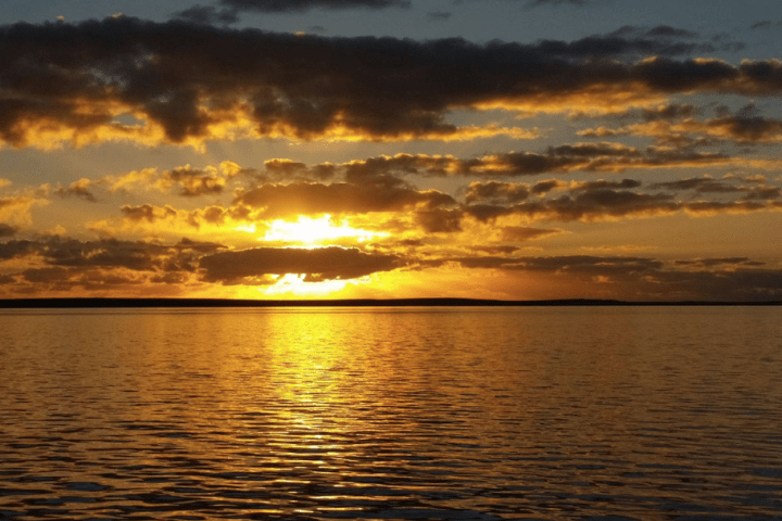 Sunset over a calm ocean with scattered clouds reflecting orange and gold hues.
