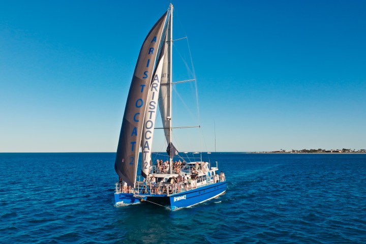 A catamaran named Aristocat 2 sailing on the open sea under a clear blue sky.