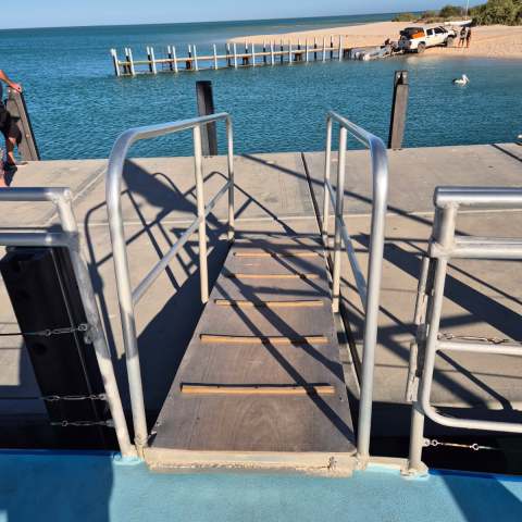Boat ramp with metal railings, water in background, sandy shore, truck, and pelican nearby.