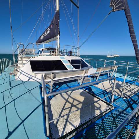 Deck view of a sailboat on the ocean under a clear blue sky.