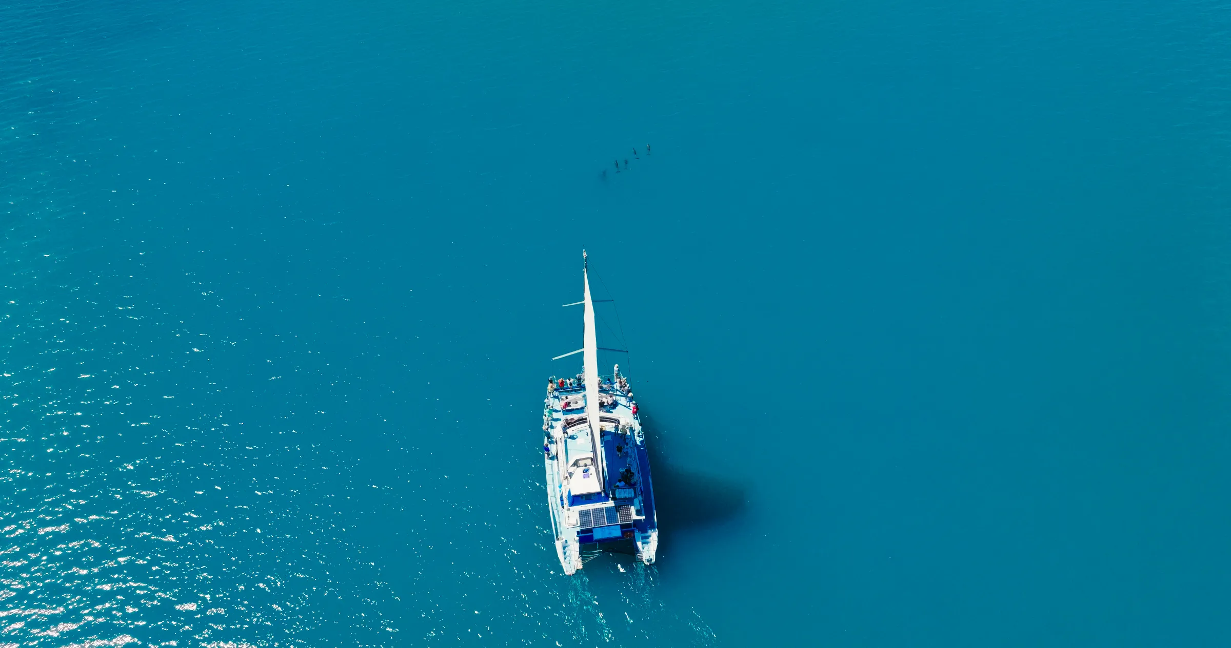 Aerial view of a boat in clear blue water with a distant shadow.