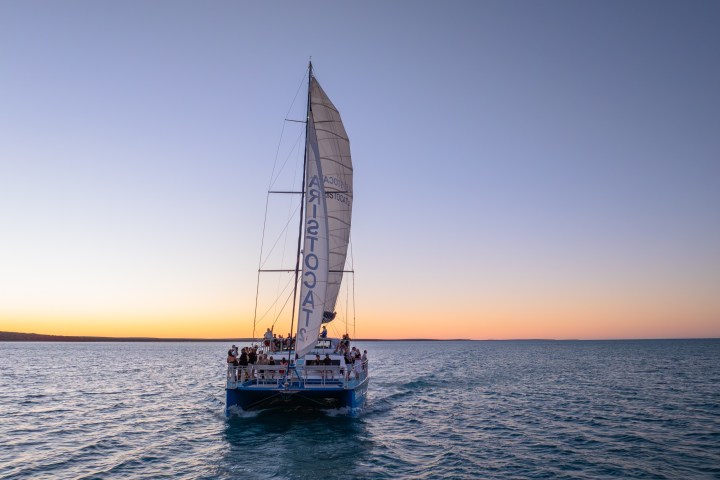 Sailboat with people sailing on calm water at sunset.