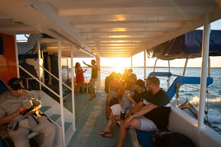 People relaxing on a boat at sunset, some sitting, some standing in groups.