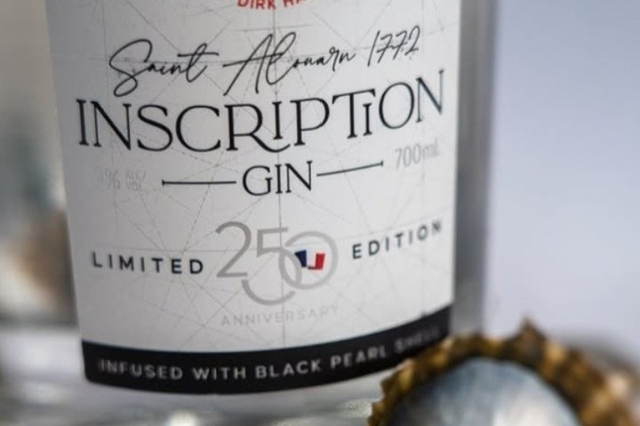 Close-up of Inscription Gin bottle label, limited edition, with a scalloped shell nearby.