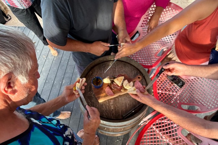 Group of people sharing snacks and drinks around a barrel table.