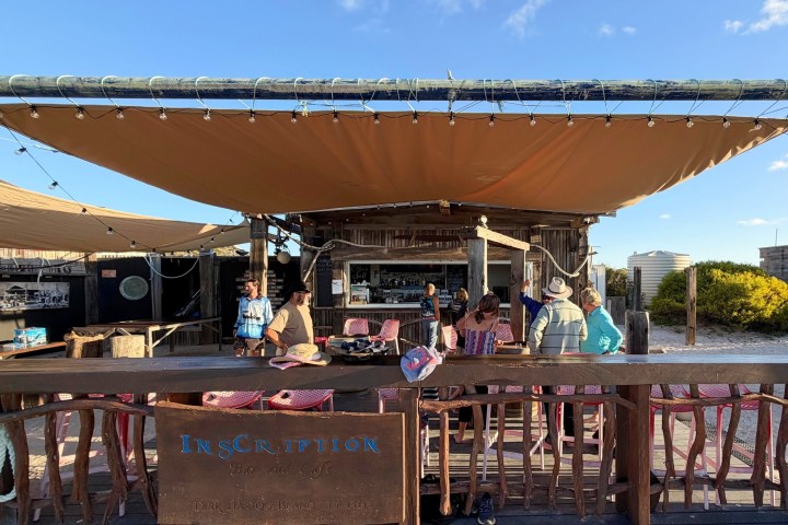 Outdoor bar with people under canvas canopy on a sunny day.